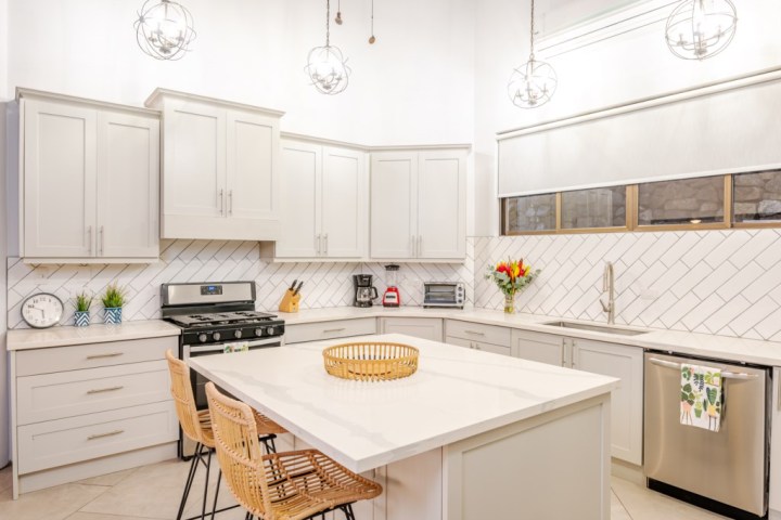 Modern kitchen with white cabinets, island, wicker chairs, and stainless appliances.