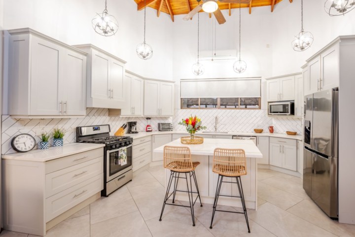 Modern kitchen with white cabinets, island, bar stools, and stainless steel appliances.