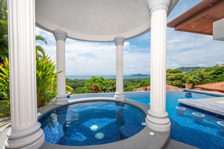 Infinity pool and hot tub with sea view, surrounded by columns and greenery.