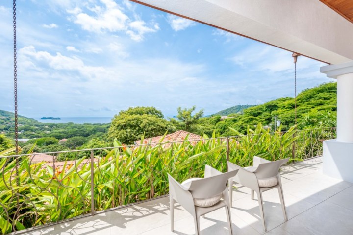 Two chairs on a balcony overlooking a lush landscape and ocean under a blue sky.