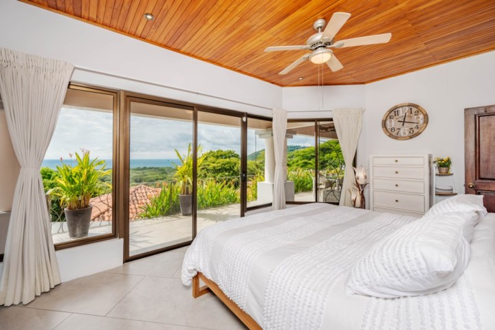 Bright bedroom with large windows, ocean view, and wooden ceiling fan.