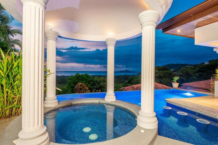 Luxurious pool with columns overlooking a scenic ocean view at dusk.