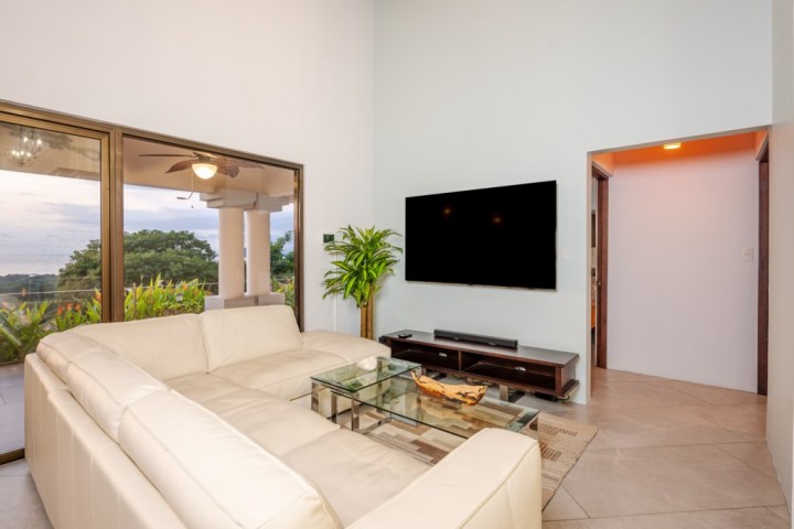 Modern living room with white sectional sofa, glass table, large TV, and sliding glass doors to patio.