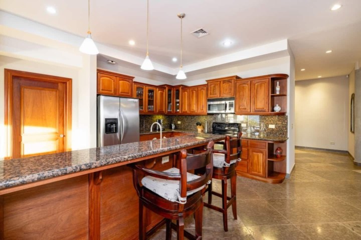 Modern kitchen with granite countertops, wooden cabinets, bar stools, stainless steel fridge and stove.