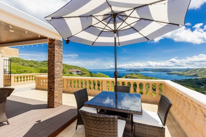 Patio with wicker chairs, a striped umbrella, and a scenic ocean view.