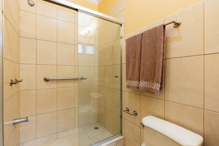 Beige tiled bathroom with glass shower door and brown towel on rack.