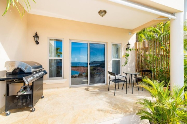 Patio with grill, table, chairs, and ocean view through sliding doors.