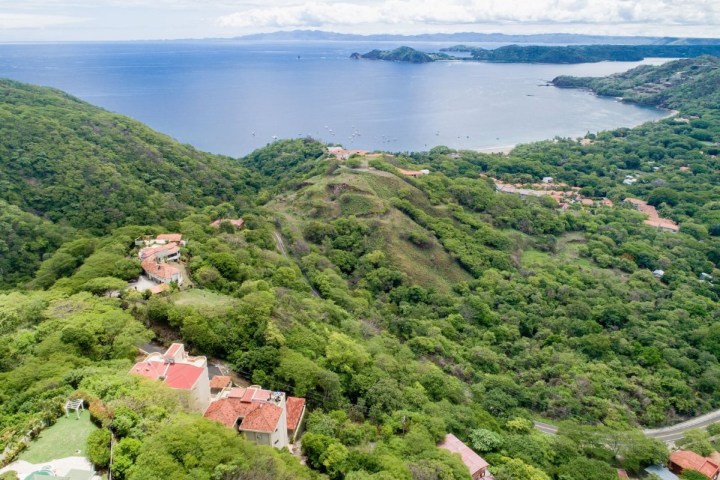 Aerial view of a coastal landscape with lush green hills and a bay.