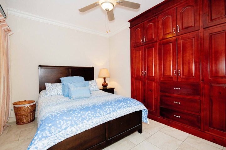 Bedroom with blue bedding, wooden closet, ceiling fan, and a table lamp.