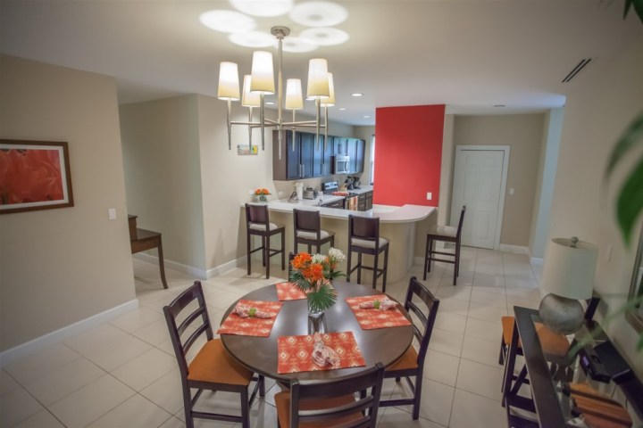 Open-plan kitchen and dining area with round table, four chairs, and a modern light fixture.