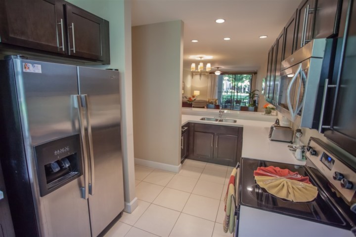 Modern kitchen with stainless steel appliances and dark cabinets, leading to a living area.
