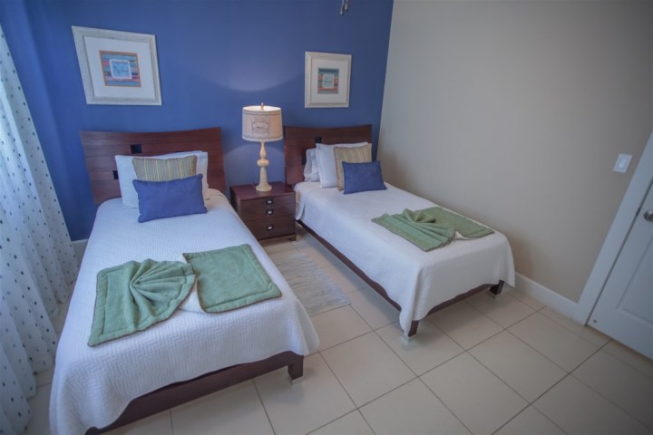 Room with two single beds, blue wall, and a bedside table with a lamp.