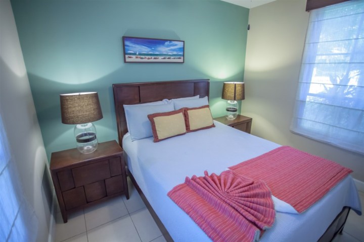 Cozy bedroom with blue accent wall, bed with pillows, lamps on side tables, and a landscape painting.