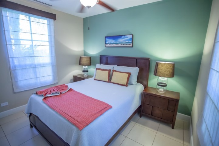 Bedroom with a bed, green accent wall, two lamps, and a landscape picture above the headboard.