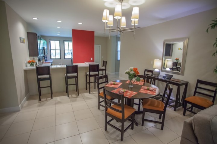 Modern dining area with round table, six chairs, bar stools, chandelier, and red accent wall.