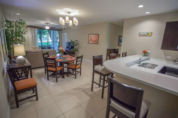 Open-plan kitchen and living area with dining table, bar stools, and sliding glass doors.