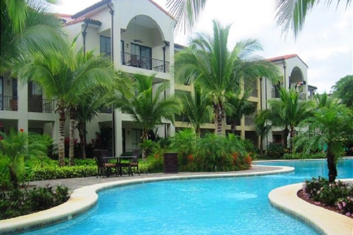 Swimming pool with palm trees and a multi-story building in the background.