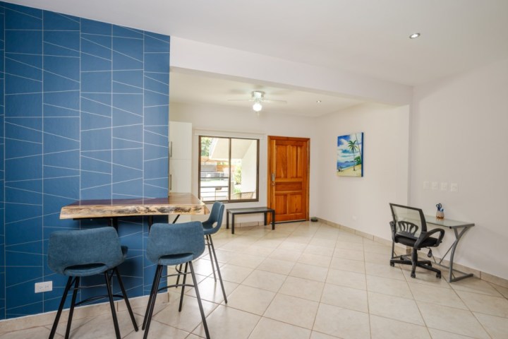 Modern room with blue accent wall, bar stools, desk, and wall art, featuring tiled floor and ceiling fan.