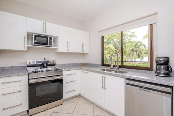 Modern kitchen with white cabinets, granite countertops, oven, microwave, coffee maker, and window view.