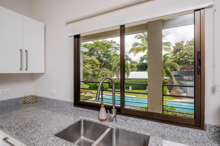 Kitchen sink with a window view of a pool and palm trees outside.