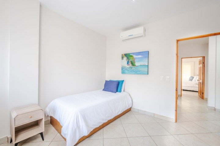 Minimalist bedroom with single bed, nightstand, artwork, and air conditioner.