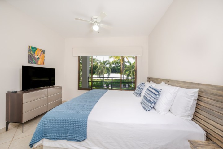 Bright bedroom with bed, TV, dresser, ceiling fan, and large window with garden view.