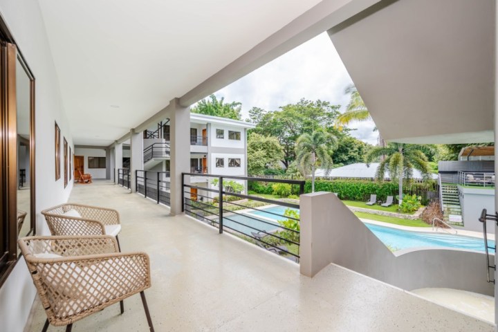 Modern balcony view, wicker chairs, overlooking pool, garden, and palm trees.