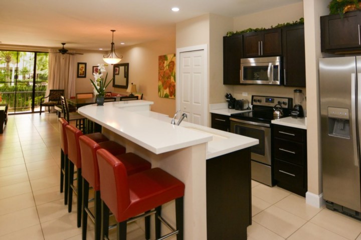 Modern kitchen and dining area with red chairs, stainless steel appliances, and a breakfast bar.