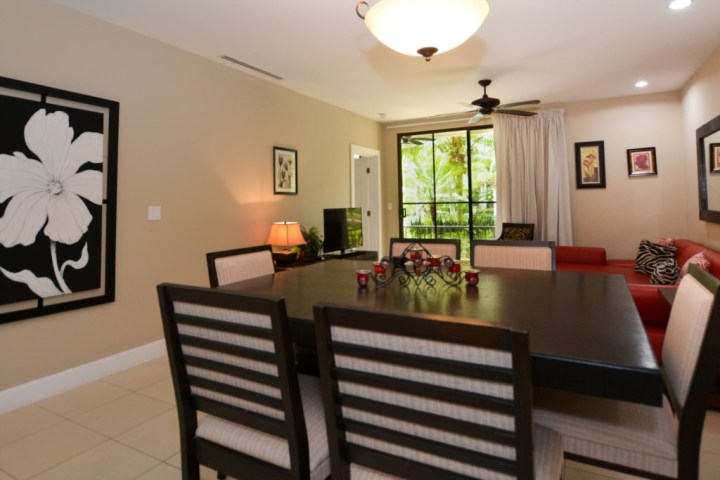 Dining and living area with a dark table, beige chairs, red sofa, and large window view with greenery.