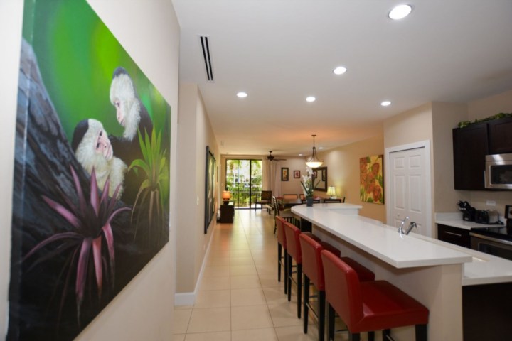 Modern kitchen with long white island, red stools, and monkey artwork on wall.