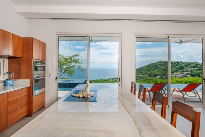 Modern kitchen with ocean view, wooden cabinets, and dining area.