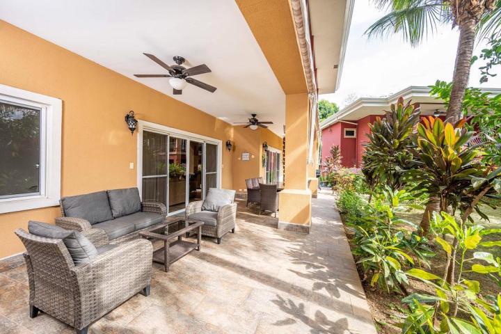 Outdoor patio with wicker furniture, ceiling fans, sliding glass doors, and tropical plants.