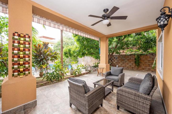 Covered patio with wicker furniture, ceiling fan, and garden view. Wall art and potted plants decorate the space.