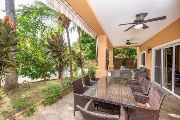 Covered patio with wicker table and chairs, ceiling fans, and view of lush garden.
