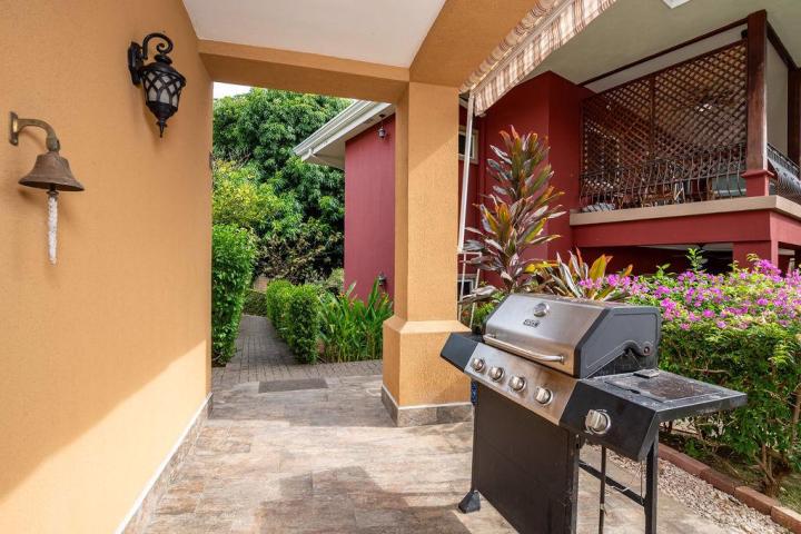 Outdoor patio with grill, potted plants, and a bell on an orange wall.
