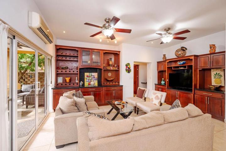 Living room with beige sofas, wooden cabinets, ceiling fans, and sliding glass doors to a patio.
