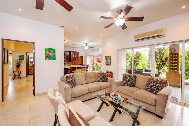 Modern living room with beige sofas, glass coffee table, ceiling fans, and large sliding glass doors to patio.