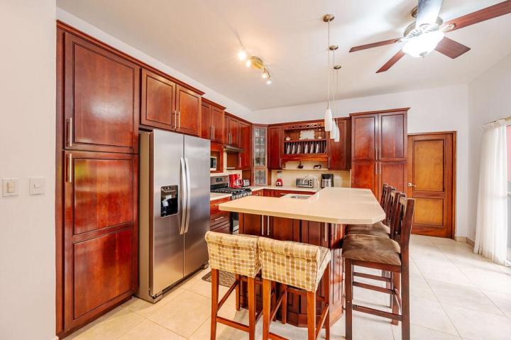 Modern kitchen with wooden cabinets, stainless steel fridge, island with bar stools, and ceiling fan.
