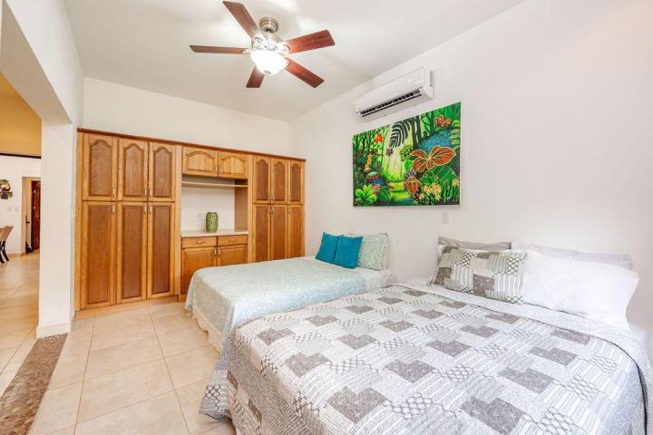 Bedroom with two beds, wooden wardrobe, ceiling fan, and colorful jungle painting on the wall.