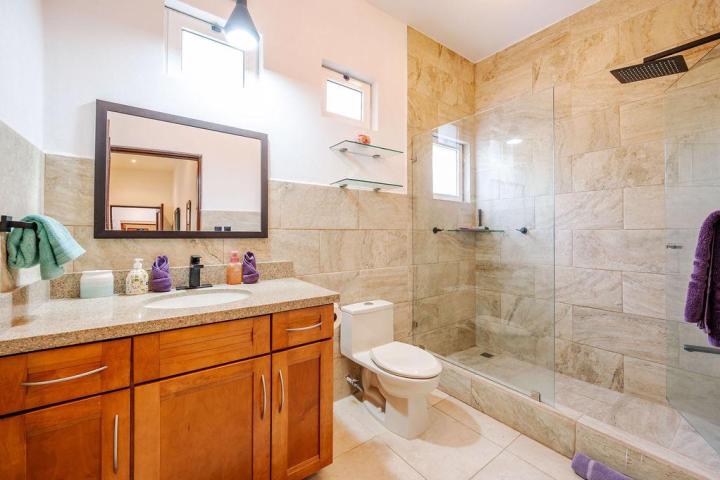 Modern bathroom with wood vanity, large mirror, glass shower, and beige tiles.