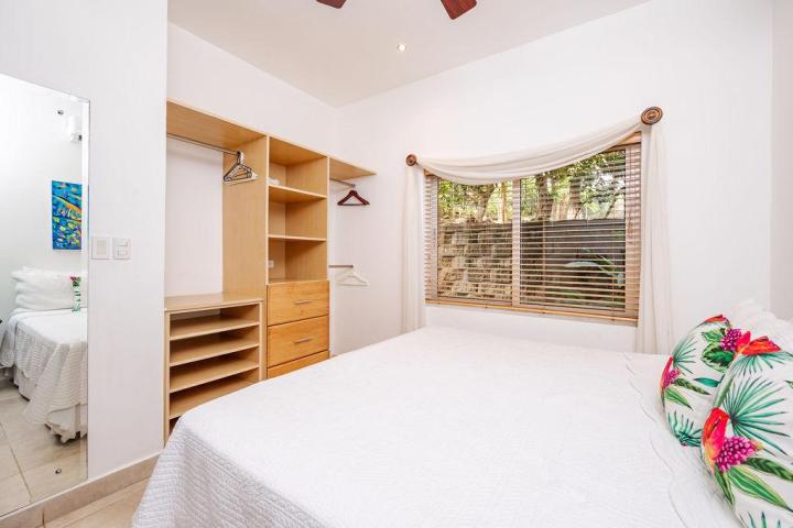 Bedroom with white bedding, tropical pillows, wooden closet, large window, and ceiling fan.
