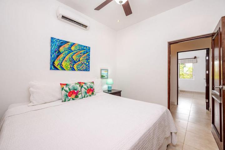 Bedroom with white bedding, colorful fish painting, floral pillows, and open door to adjacent room.