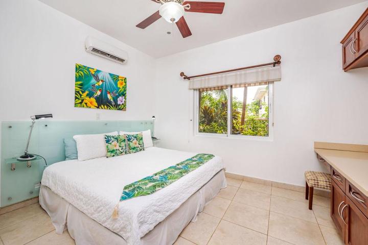 Bright bedroom with king bed, colorful artwork, ceiling fan, and window view of greenery.