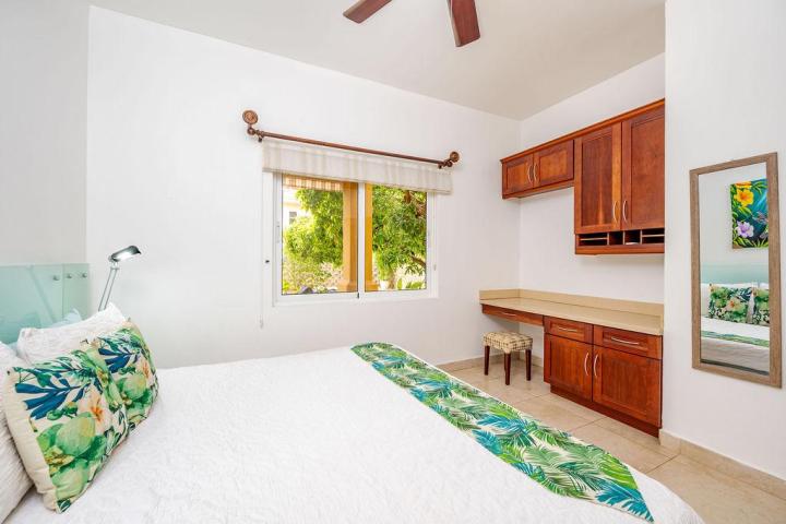 White bedroom with floral bedspread, wooden cabinets, window view of greenery, and wall mirror.