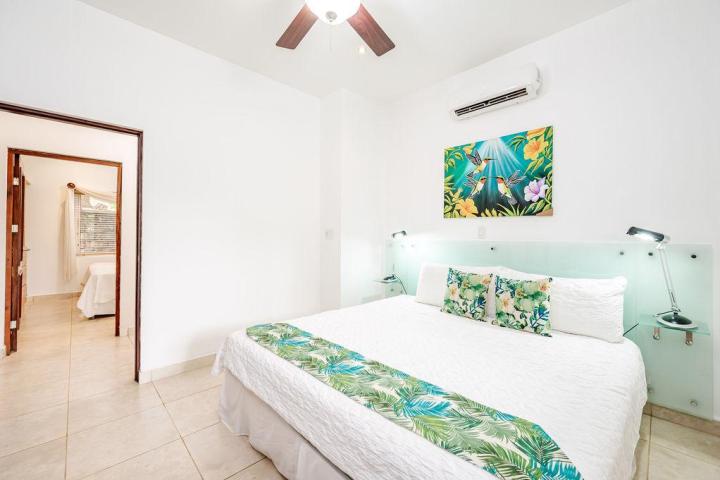 Bright bedroom with white bed, floral decor, ceiling fan, and open door to another room.