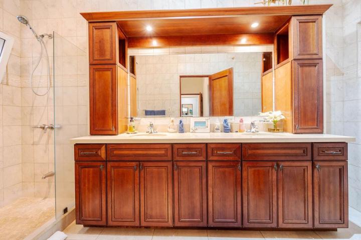 Bathroom with wooden vanity, twin sinks, large mirror, and walk-in shower.