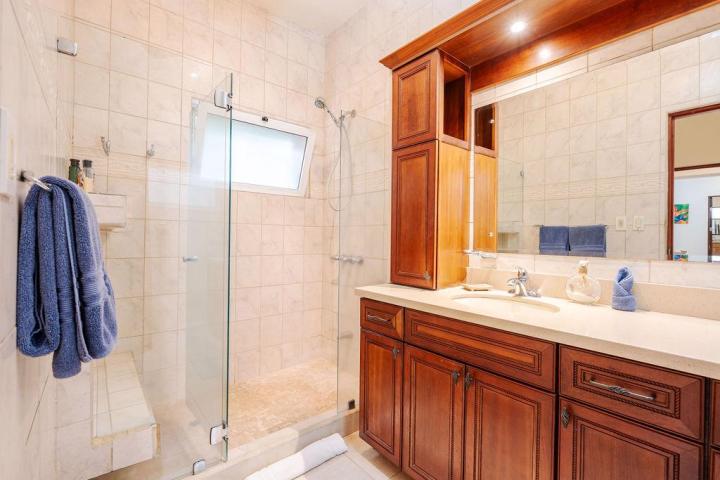 Bathroom with wood cabinets, glass shower door, blue towels, and beige tiles.