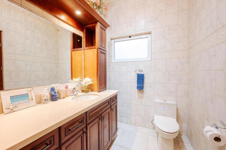 Bathroom with wooden vanity, sink, mirror, toilet, and tiled walls.