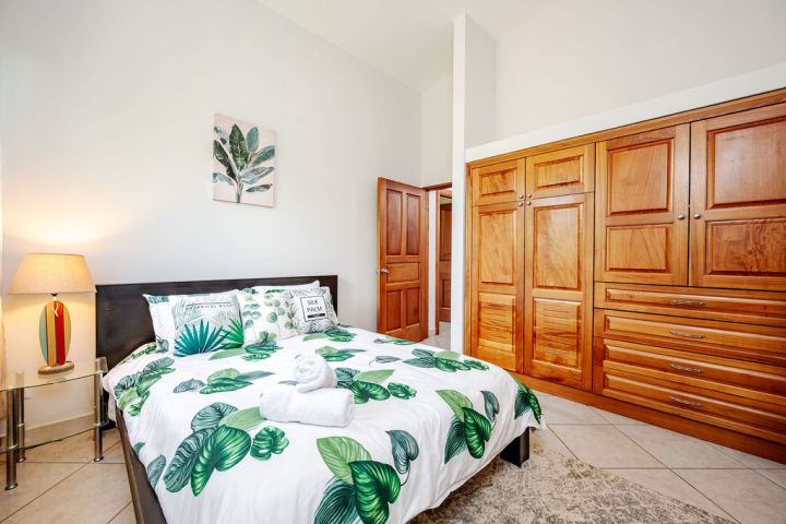 Bedroom with leafy bedding, wooden wardrobe, lamp, and framed leaf artwork on wall.