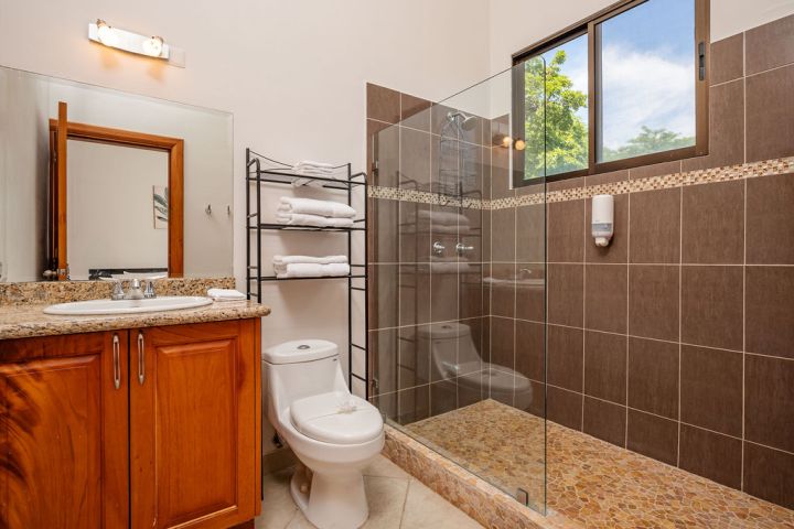 Modern bathroom with wooden vanity, glass shower, towel rack, and window view.